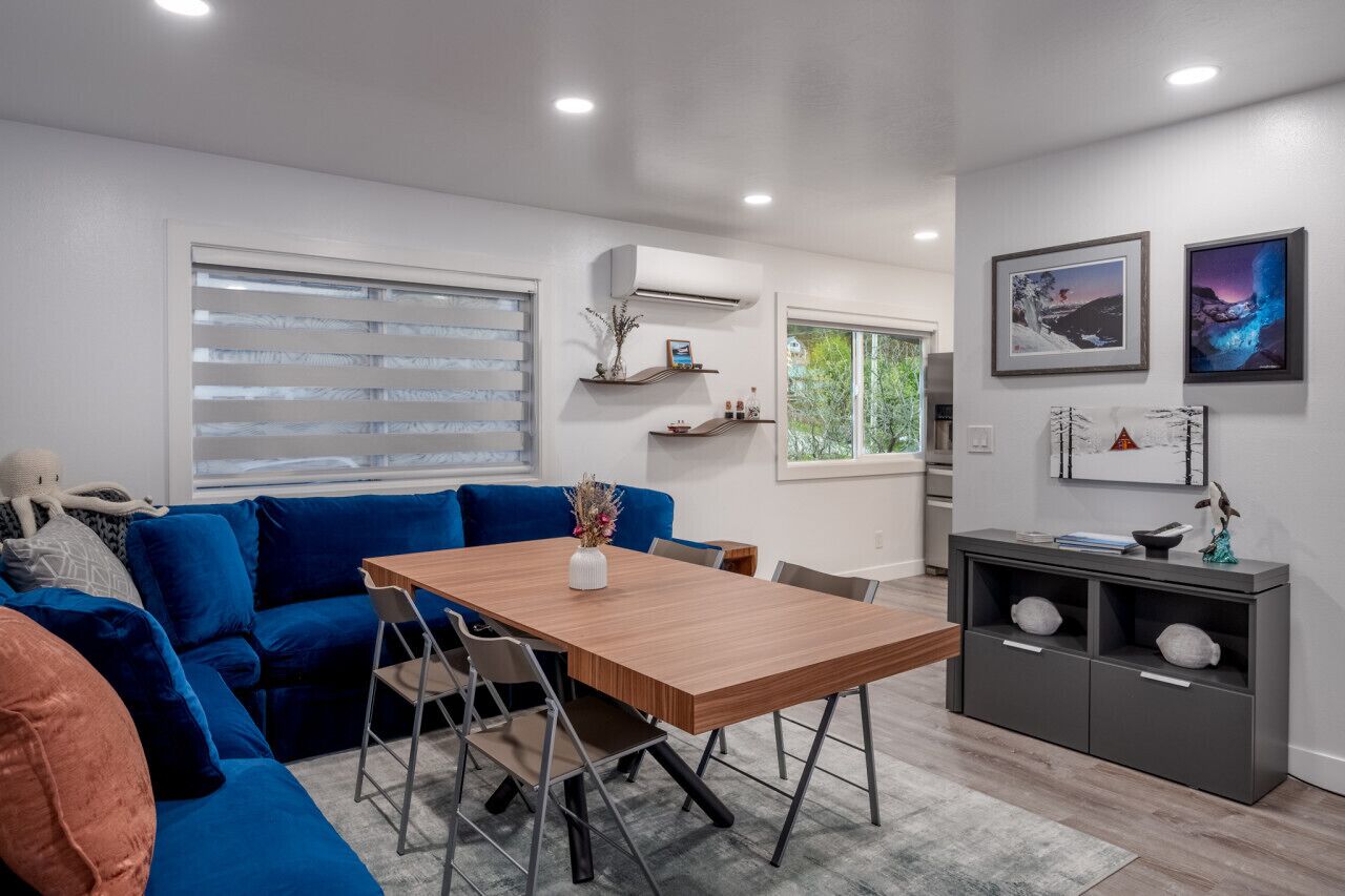 A modern living room with a blue sofa, a wooden dining table, and a grey cabinet with shelves.