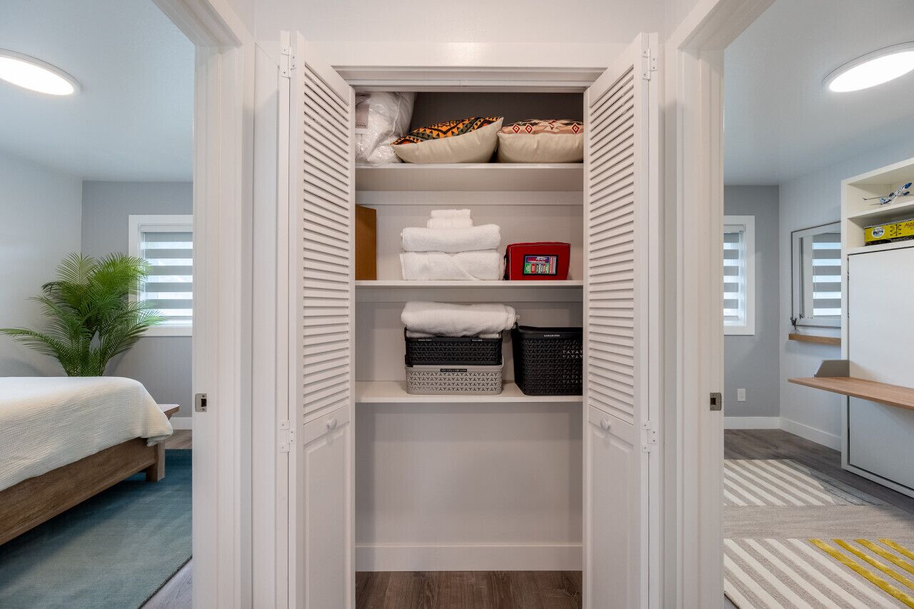 A walk-in closet with shelves, a bed, and a plant.