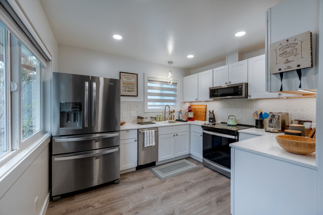 A modern kitchen with stainless steel appliances, white cabinetry, and a large window providing natural light.