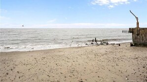 En strand med en trækonstruktion til højre, klar himmel og rolig sø.