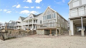 En ejendom ved stranden med flere huse, en sandstrand og et træhegn.