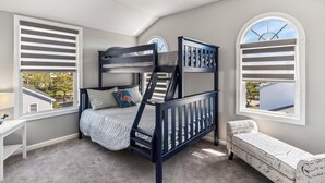 A bunk bed with a headboard, a bedside table, and a window with shutters.
