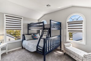 A bunk bed with a headboard, a bedside table, and a window with shutters. - Bayside Retreat in Bethany Beach: Short Walk to Beach, Sleeps 13, Water Views! (Bethany Beach)