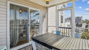 A covered outdoor area with a table and chairs, a sliding glass door, and a view of neighboring houses.