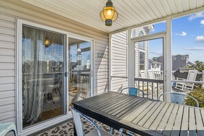 A covered outdoor area with a table and chairs, a sliding glass door, and a view of neighboring houses. - Bayside Retreat in Bethany Beach: Short Walk to Beach, Sleeps 13, Water Views! (Bethany Beach)