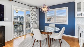 A modern kitchen with white cabinets, a round dining table with white chairs, and a large window with blinds.