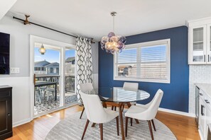 A modern kitchen with white cabinets, a round dining table with white chairs, and a large window with blinds. - Bayside Retreat in Bethany Beach: Short Walk to Beach, Sleeps 13, Water Views! (Bethany Beach)