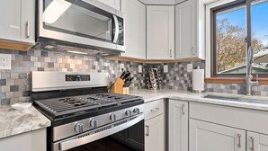 Une cuisine moderne avec des armoires blanches, une cuisinière en acier inoxydable, un four à micro-ondes et une fenêtre donnant sur les arbres.