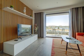 Relax in a stylish living room with a flat-screen TV, glass coffee table, and comfortable sofa, offering a view of the coastal landscape.