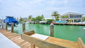 A wooden dock with a bench, a covered boat, and a building with a balcony overlooking a marina. - Pool, Key Colony Beach, Dock, Across from the Golf Course (Key Colony Beach)