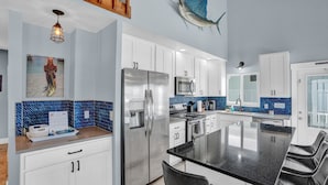 A modern kitchen with white cabinets, a stainless steel refrigerator, a microwave, and a blue tiled backsplash. - Pool, Key Colony Beach, Dock, Across from the Golf Course (Key Colony Beach)