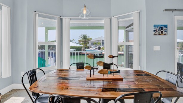A dining area with a wooden table, chairs, and a view of the marina through large windows. - Pool, Key Colony Beach, Dock, Across from the Golf Course (Key Colony Beach)