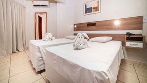 Een hotelkamer met twee bedden, een houten hoofdbord, een nachtkastje en een aan de muur bevestigde airconditioner.
