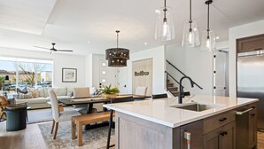 A modern kitchen with a large island, pendant lights, and a stainless steel refrigerator.