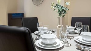 A dining table set with white plates, bowls, and glasses, surrounded by black chairs. - 3BR Waterfront Apt - 10 min to City Center Ipswich (Ipswich)