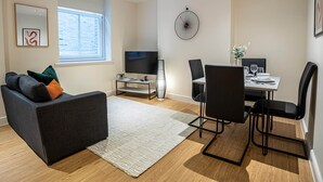 A modern living room with a sofa, TV, and dining area. - 3BR Waterfront Apt - 10 min to City Center Ipswich (Ipswich)