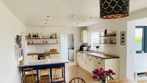 A spacious kitchen with a central island, wooden dining table, and chairs. There are shelves with kitchenware and a microwave on the countertop. - Beautiful 4-bed House With Countryside Views (Haverfordwest)