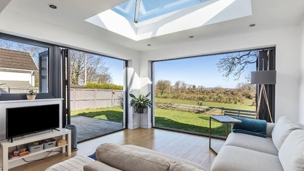 A modern living room with a large TV, comfortable seating, a skylight, and a view of a grassy area. - Beautiful 4-bed House With Countryside Views (Haverfordwest)