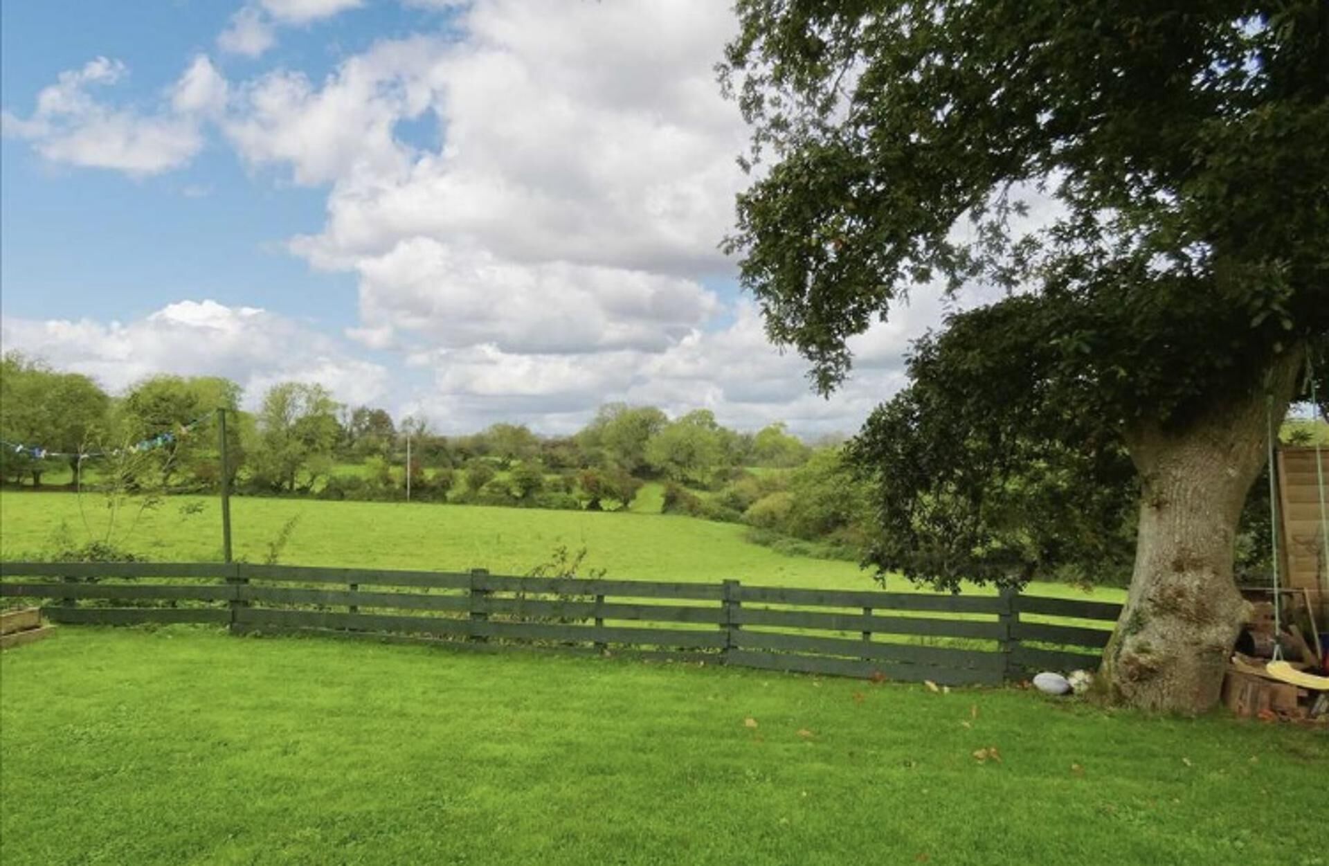 A grassy field with a wooden fence and a large tree.