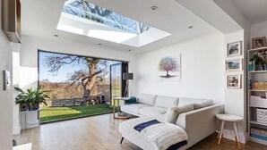 A modern living room with a large glass door leading to a garden, a sofa, a small table, and a bookshelf. - Beautiful 4-bed House With Countryside Views (Haverfordwest)