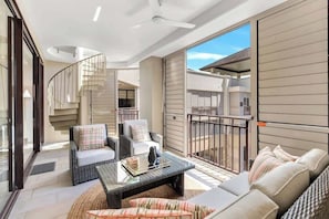 A modern living room with a glass coffee table, wicker furniture, and a spiral staircase.