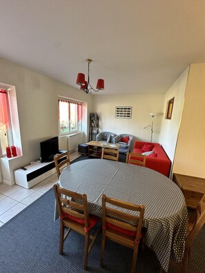 A living room with a round dining table, two wooden chairs, a red sofa, a television, and a bookshelf. - Ground floor, balcony, tv, 50m², Villard de Lans (Villard-de-Lans)