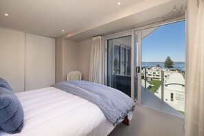 A bedroom with a bed, a chair, a balcony with a view of buildings and water.