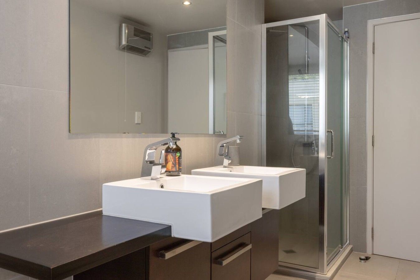A modern bathroom with two sinks, a large mirror, and a glass shower enclosure.