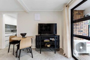 A modern living room with a dining area, a flat-screen TV, and a large window with a view of a brick building.