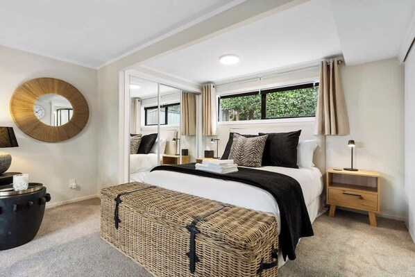 A bedroom with a bed, bedside tables, a mirror, a window, and a circular wall decoration.