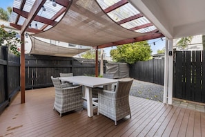 A covered patio area with a table and chairs, a wooden deck, and a black fence in the background. - 1-bed wow factor in Kohimarama (Auckland)
