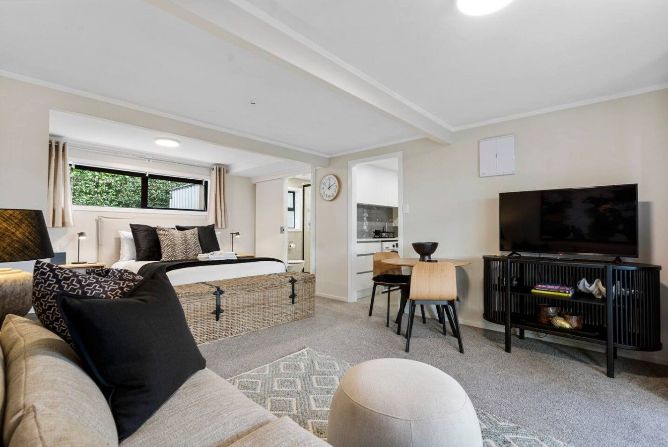Una habitación moderna y bien iluminada con una cama, zona de comedor, televisor y kitchenette.
