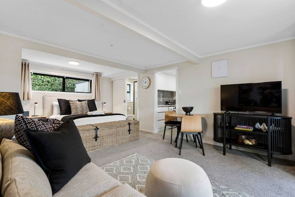 A modern, well-lit room with a bed, a dining area, a TV, and a kitchenette. - 1-bed wow factor in Kohimarama (Auckland)
