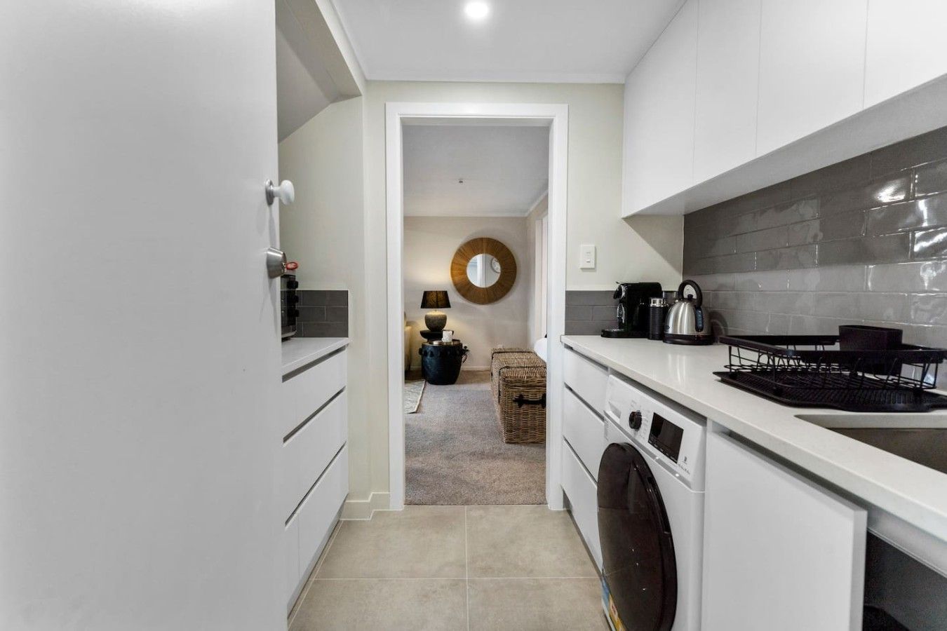 A modern kitchen with white cabinetry, a built-in oven, and a coffee machine.