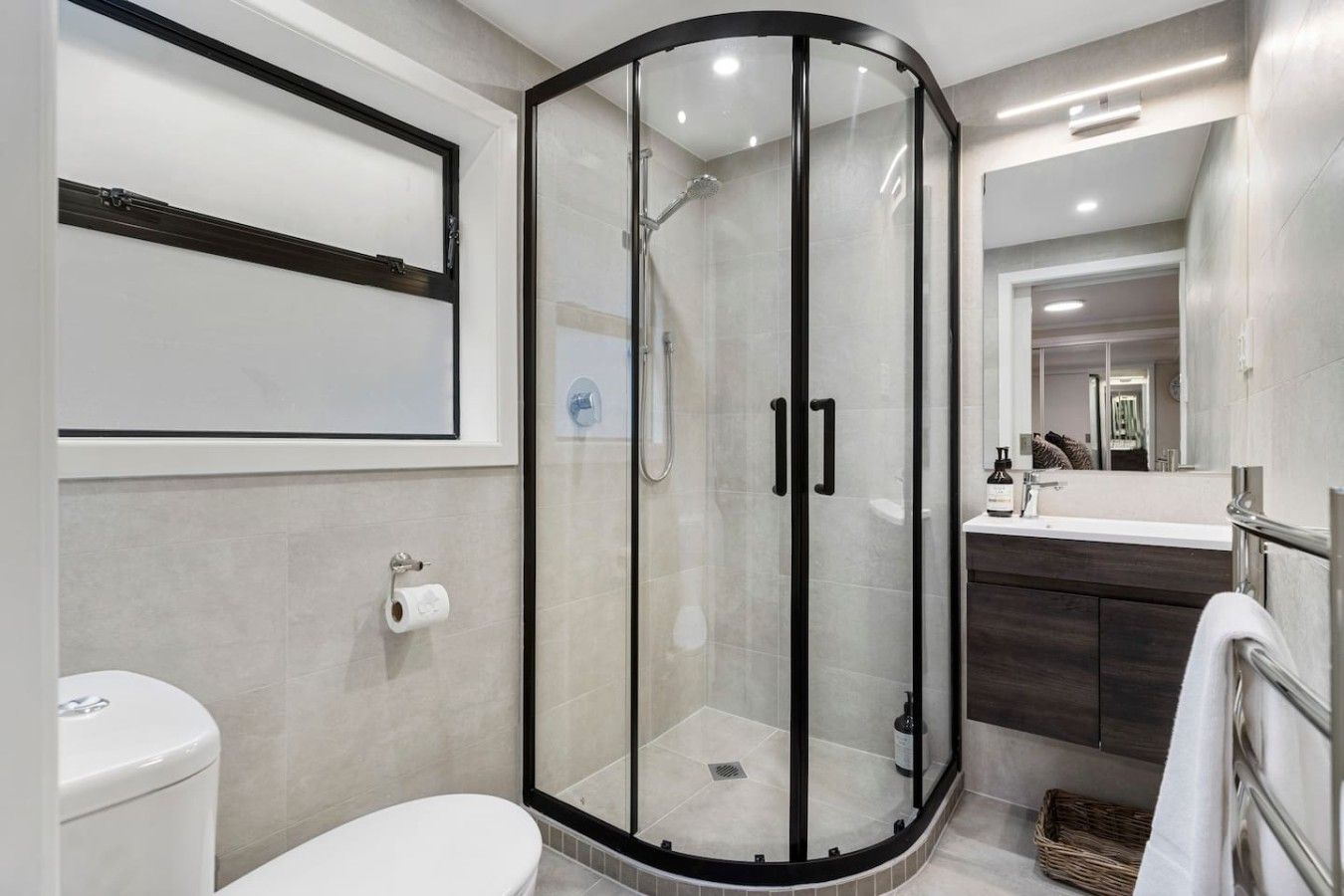 A modern bathroom with a glass-enclosed shower, a toilet, and a vanity with a mirror.