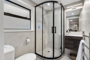 A modern bathroom with a glass-enclosed shower, a toilet, and a vanity with a mirror. - 1-bed wow factor in Kohimarama (Auckland)