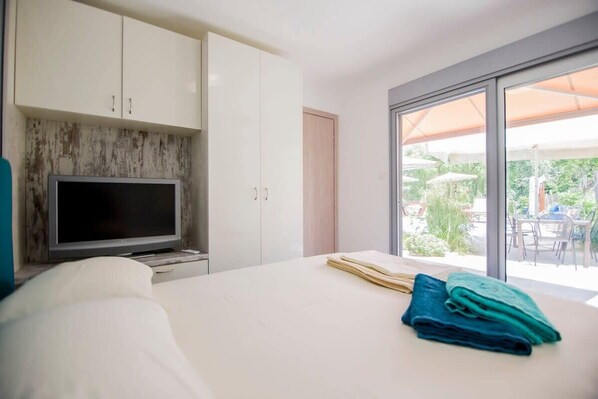 A bedroom with a bed, a TV, and a view of an outdoor patio.