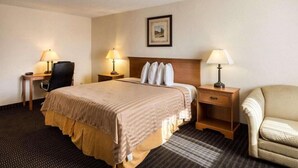 A hotel room with a bed, two bedside tables with lamps, a chair, and a framed picture on the wall.
