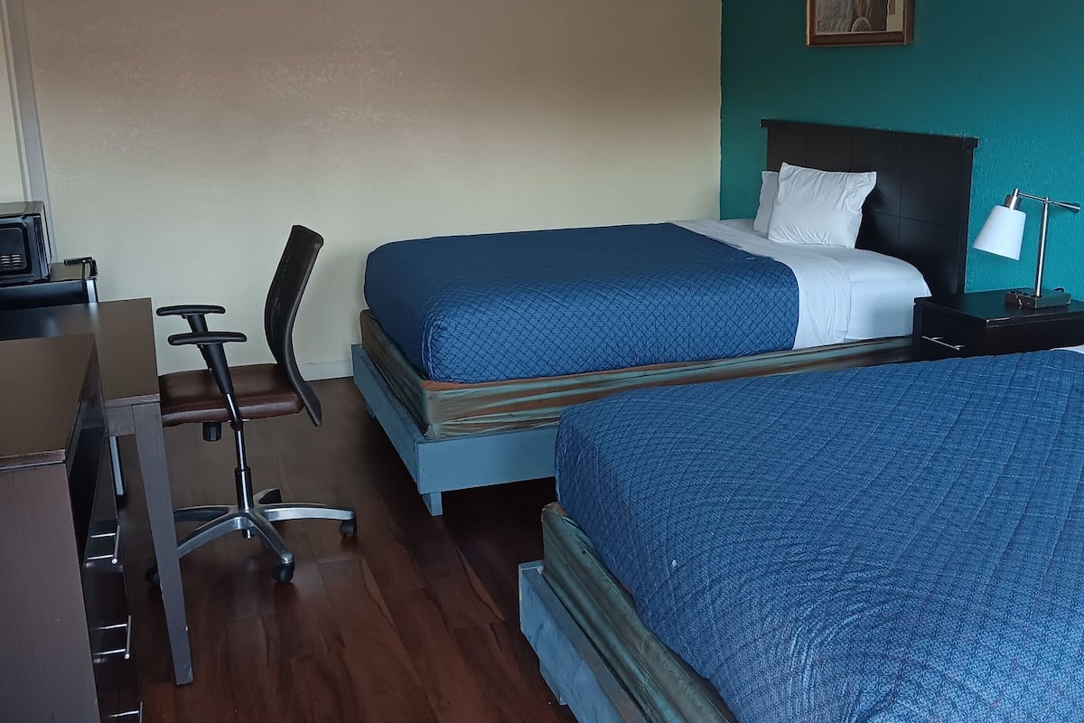 A hotel room with two beds, a desk with a computer, a chair, and a TV.