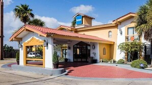 A hotel with a red-tiled entrance, a covered waiting area, and a clear blue sky.