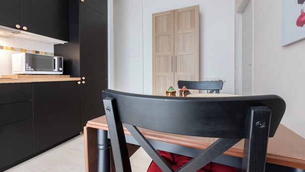 A modern kitchen with black cabinets, a white microwave, and a wooden dining table with chairs. - Italianway - Cermenate 7 (Milan)