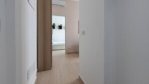 A narrow hallway with a wooden door, a white wall, and a bed in the background. - Italianway - Cermenate 7 (Milan)