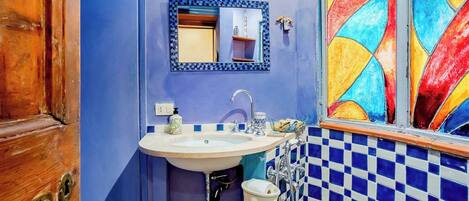 A bathroom with a blue tiled wall, a white sink with a mirror above it, and a colorful window.