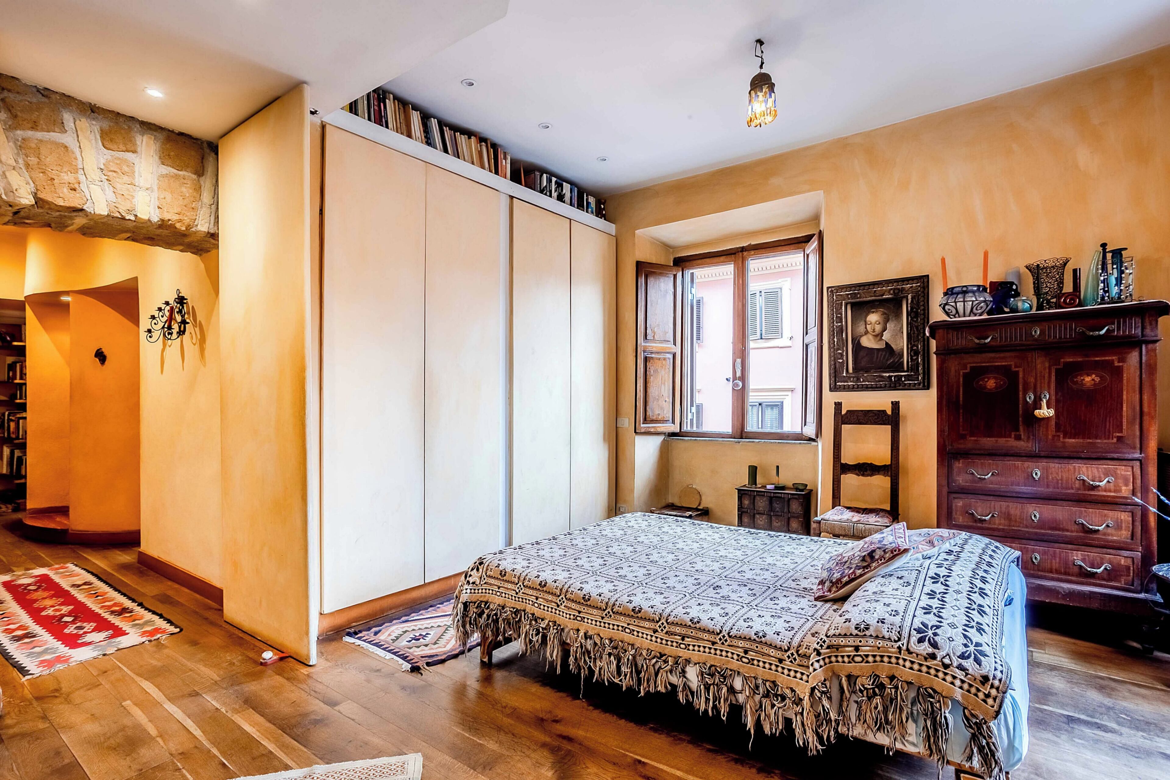 A bedroom with a large bed, wooden wardrobe, and a window with a view.