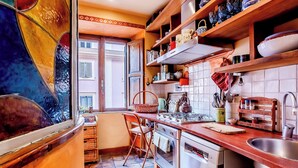 A kitchen with a stove, sink, and cabinets. There is a window with shutters and a chair. - Lovely 2-bed Apartment in Roma (Rome)