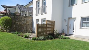 A modern building with a stone wall, a wooden fence, and a well-maintained lawn. - Ferienwohnung Hansen, in Ruhiger Lage mit Wunderschönem Ausblick (Welschbillig)