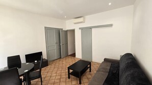 A living room with a sofa, a coffee table, a dining table with chairs, and a wardrobe. - Studio Climatisé Intra Muros Secteur Vernet Calme et Lumineux (Avignon)