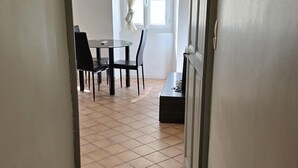 A hallway leading to a dining area with a table and chairs, a window with curtains, and a radiator on the wall. - Studio Climatisé Intra Muros Secteur Vernet Calme et Lumineux (Avignon)