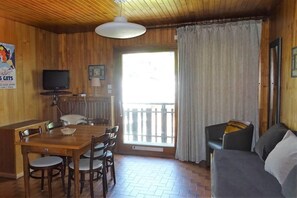A wooden interior with a dining table, chairs, a sofa, a television, and a window with curtains.