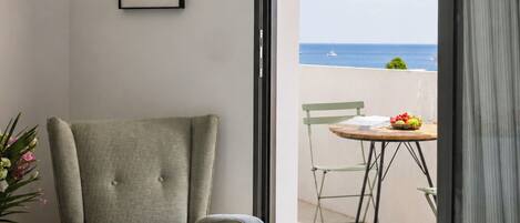 A room with a bed, a chair, a table with fruit, and a view of the sea.
